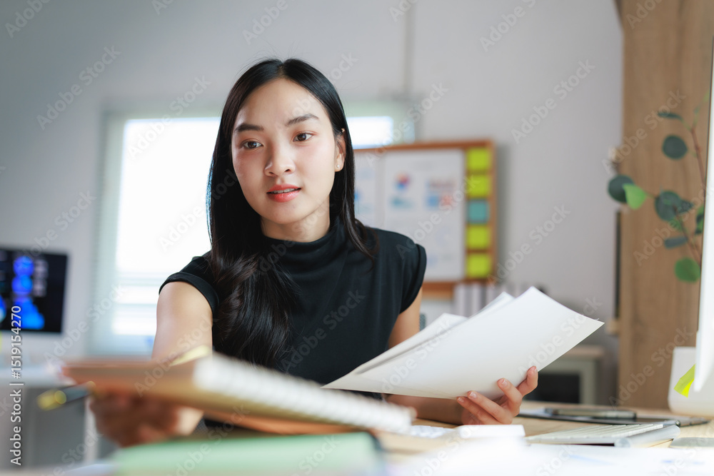 Asian businesswoman holding documents and notebook at office desk Asian businesswoman holding documents and notebook at office desk