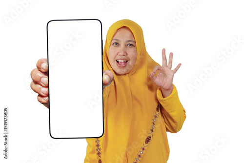 Cheerful hijabi woman shows smartphone screen and makes OK sign with happy expression