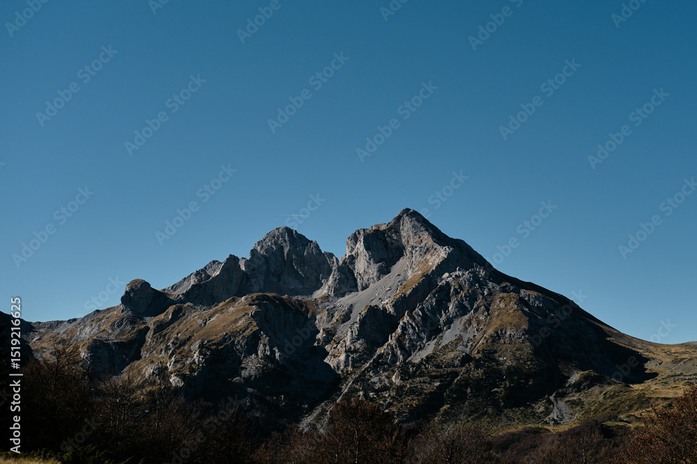Dramatic rocky peak of Komovi mountain range in Montenegro under a clear blue sky. Majestic and rugged alpine scenery captured in crisp autumn light. Dramatic rocky peak of Komovi mountain range in Montenegro under a clear blue sky. Majestic and rugged alpine scenery captured in crisp autumn light.