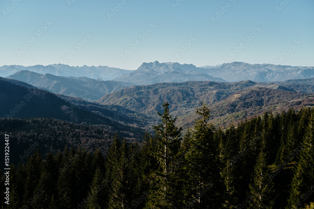 A scenic autumn landscape in the Komovi mountains of Montenegro, featuring layers of forested hills and distant rocky peaks under a clear blue sky. A scenic autumn landscape in the Komovi mountains of Montenegro, featuring layers of forested hills and distant rocky peaks under a clear blue sky.