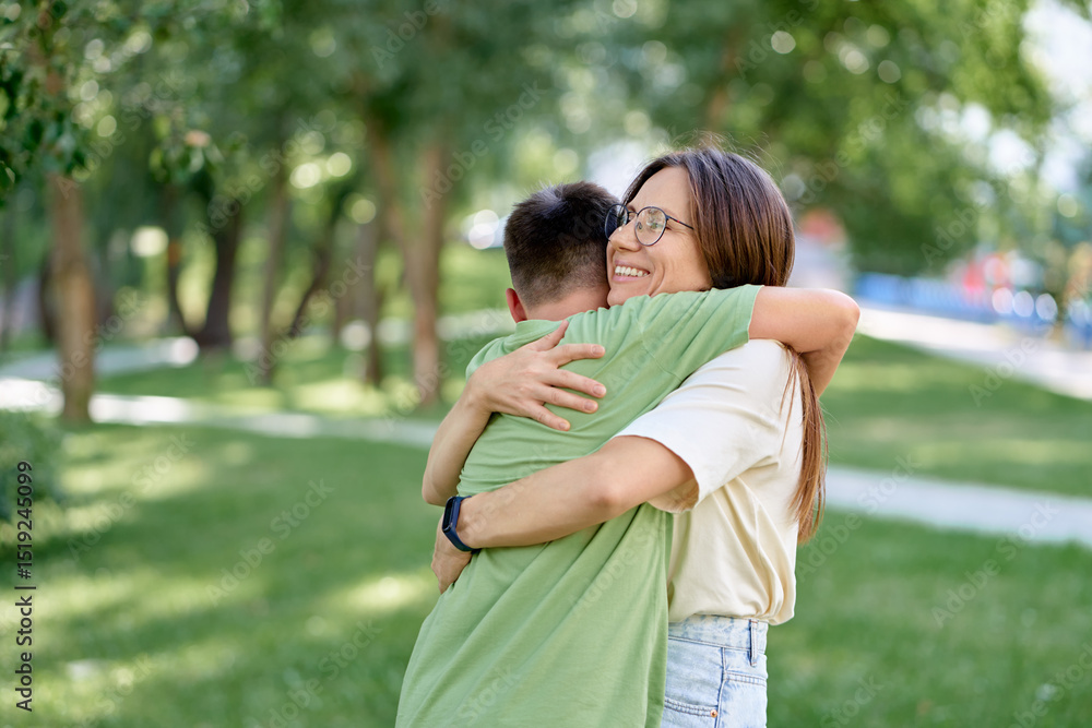 Fototapeta premium Mother Hugging Son in a Sunny Park with Greenery All Around.