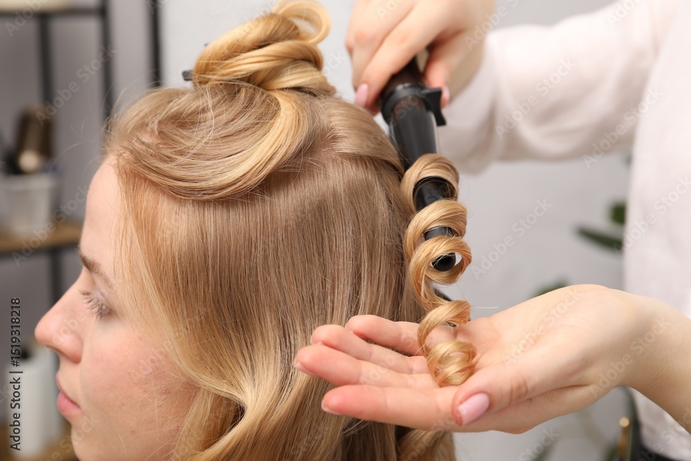 Fototapeta premium Hairdresser curling woman's hair in salon, closeup
