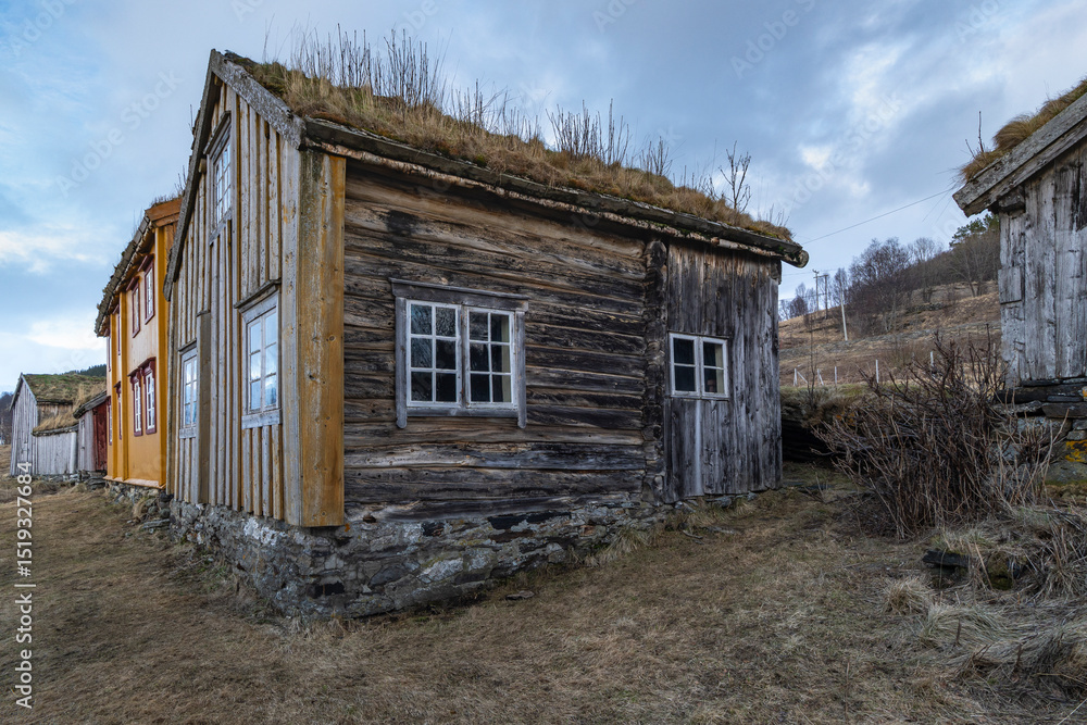 Obraz premium Norwegian old village on the fjord on the island of Kvaløya. open-air museum, old houses, landscape on the shore of Atlantic. steep snowy mountain on the roadside. We travel through Troms, Norway