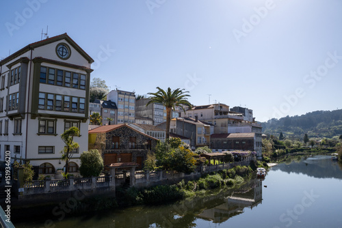 Scenic view of Ponte Vella bridge over Mandeo River in Betanzos, Galicia, Spain, surrounded by lush greenery and historic architecture.