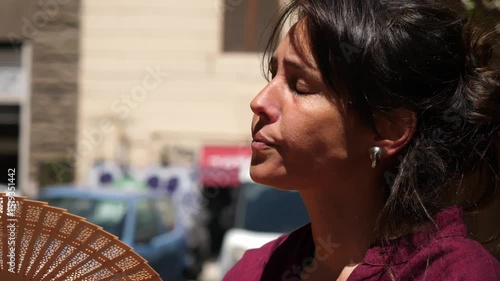 A visibly exasperated young woman uses a hand fan to fight the unbearable heat of summer