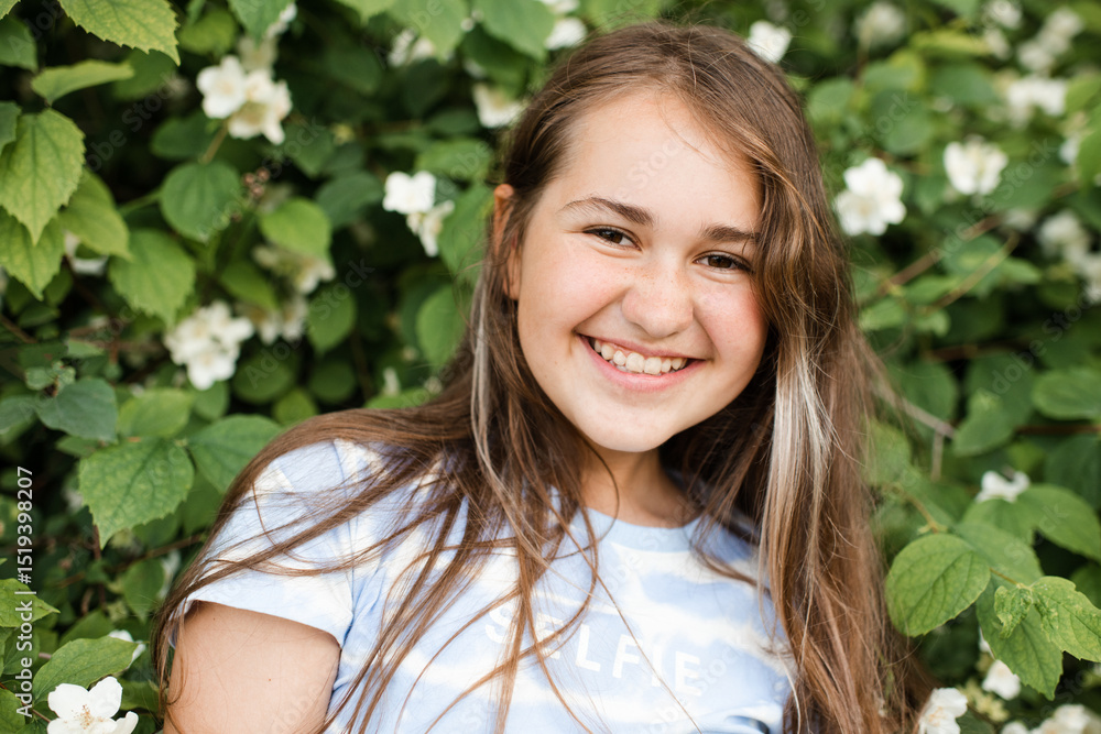 Smiling teenage girl 13 -14 year old with long healthy blonde hair over blooming jasmine bush with white flowers in garden outdoors. Happiness. Smiling teenage girl 13 -14 year old with long healthy blonde hair over blooming jasmine bush with white flowers in garden outdoors. Happiness.