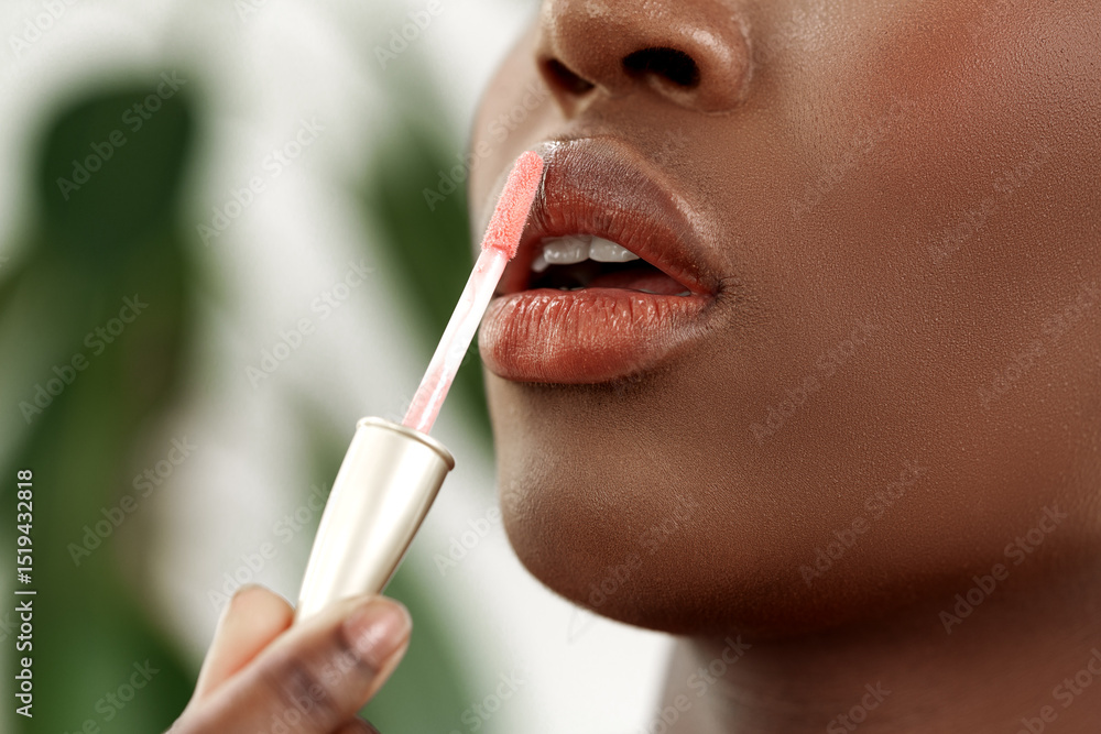 Naklejka premium Woman applying lip gloss in a natural setting with greenery in the background during daylight hours