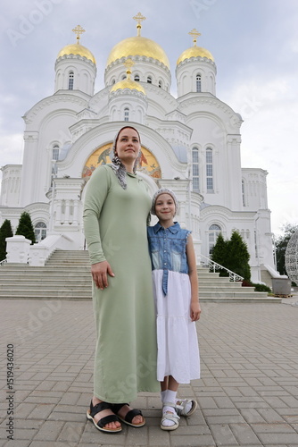 Russian woman in a scarf with a little daughter against the background of an Orthodox church