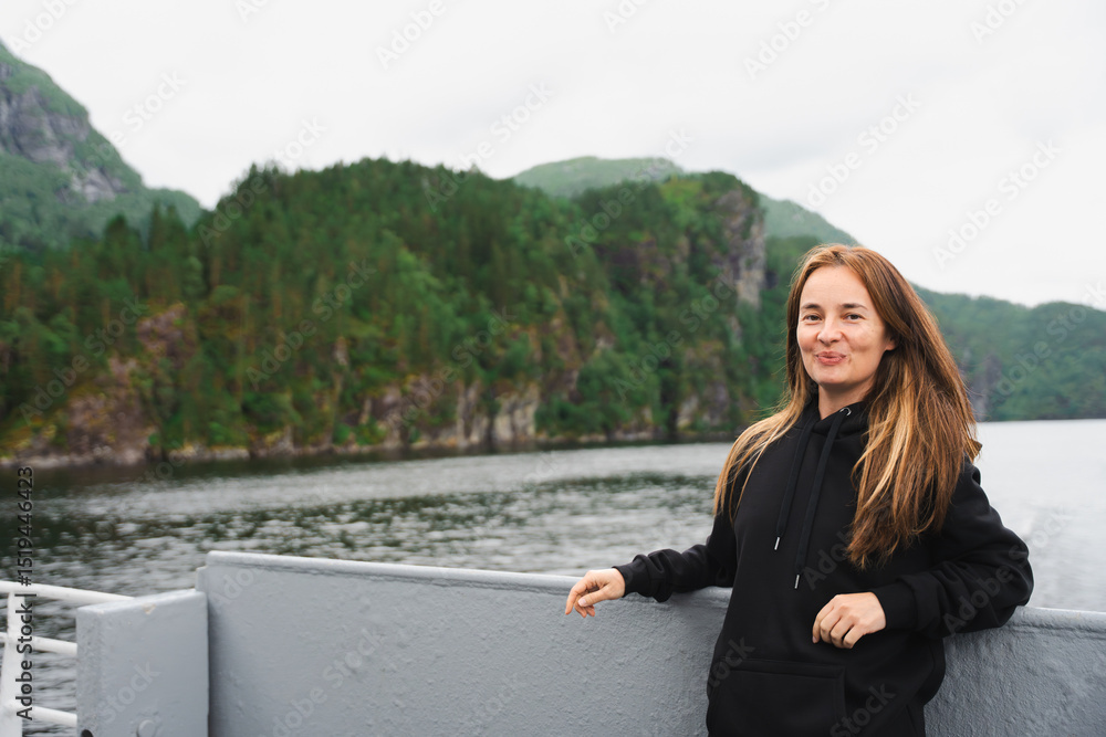 Portrait of woman with air touch hair standing on ferry in scenic fjord near Bergen, Norway. Summer day, overcast sky, green mountains and calm water in soft natural light. Confident and relaxed look Portrait of woman with air touch hair standing on ferry in scenic fjord near Bergen, Norway. Summer day, overcast sky, green mountains and calm water in soft natural light. Confident and relaxed look