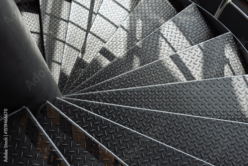 Foto Curved metal staircase with textured diamond plate steps spirals downward, illuminated by soft daylight and dynamic shadows in a modern industrial interior