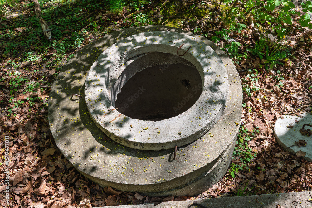 Old concrete well ring lies uncovered in the forest, surrounded by dry leaves and dappled sunlight, evoking rural utility and neglect. Old concrete well ring lies uncovered in the forest, surrounded by dry leaves and dappled sunlight, evoking rural utility and neglect.
