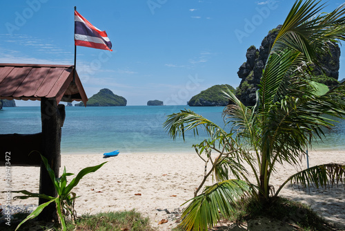 Landscape photo of a tropical beach in Thailand in the Mu Ko Ang Thong Marine Park near Koh Samui. You can see the Thai flag waving in the air, beautiful white sand, lush vegetation in the distance