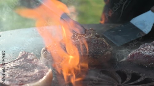 Close-up of juicy ribeye steaks being flipped over open flame on hot grill plate – barbecue cooking scene