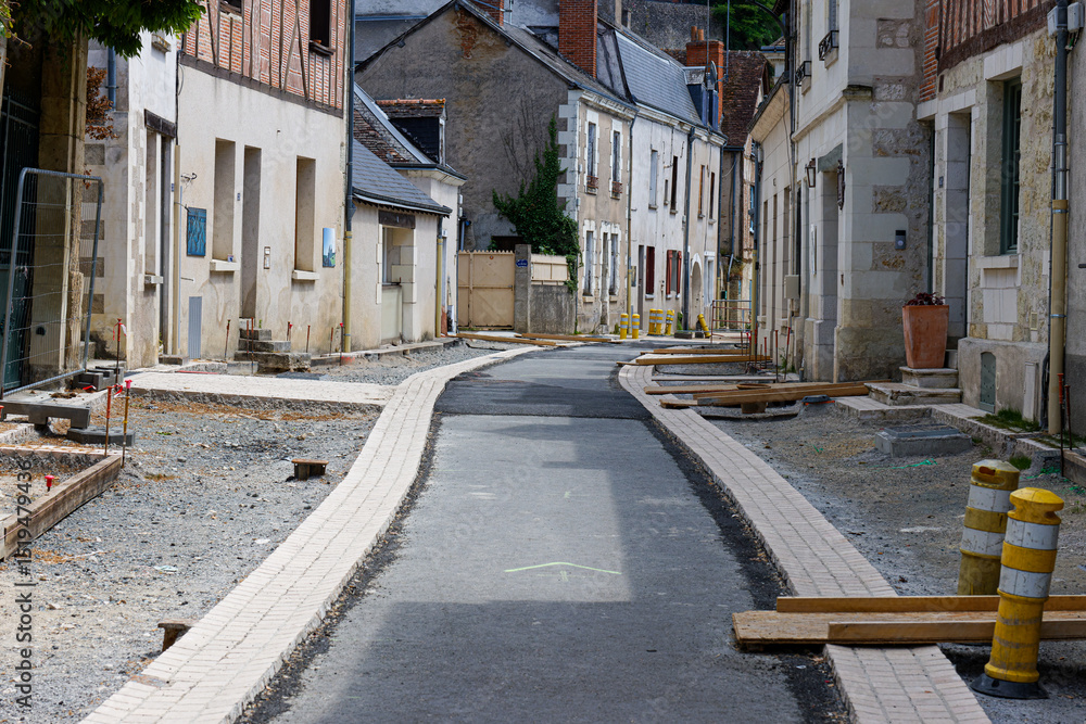 Fototapeta premium Narrow street under construction in a European town, with old buildings lining the sides and construction materials scattered around.