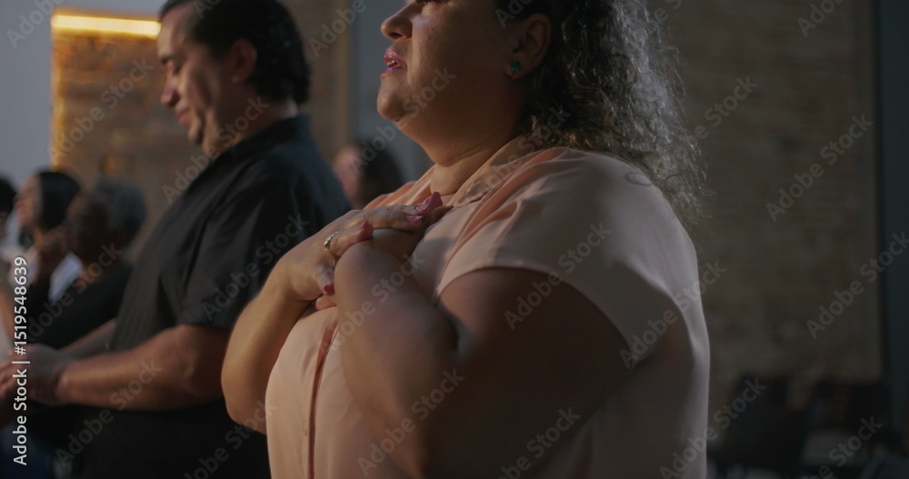 Woman with raised hand and closed eyes in prayerful moment during diverse group worship, illuminated cross in background, spirituality and connection emphasized Woman with raised hand and closed eyes in prayerful moment during diverse group worship, illuminated cross in background, spirituality and connection emphasized