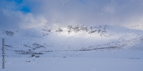 illuminated rocky mountains in the glacier-made valley, snow-covered landscape in solitude, panorama in winter wonderland Norway, with haze and fog on cloudy day, wide white snow