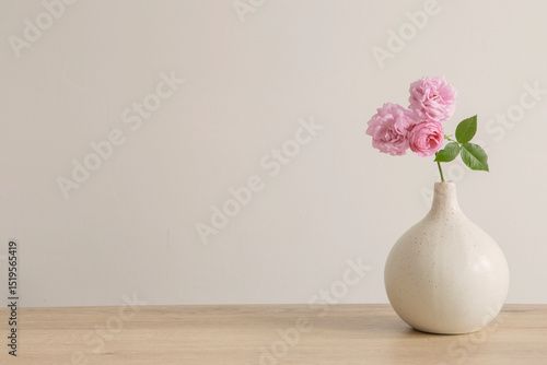 pink roses in ceramic vase on wooden table