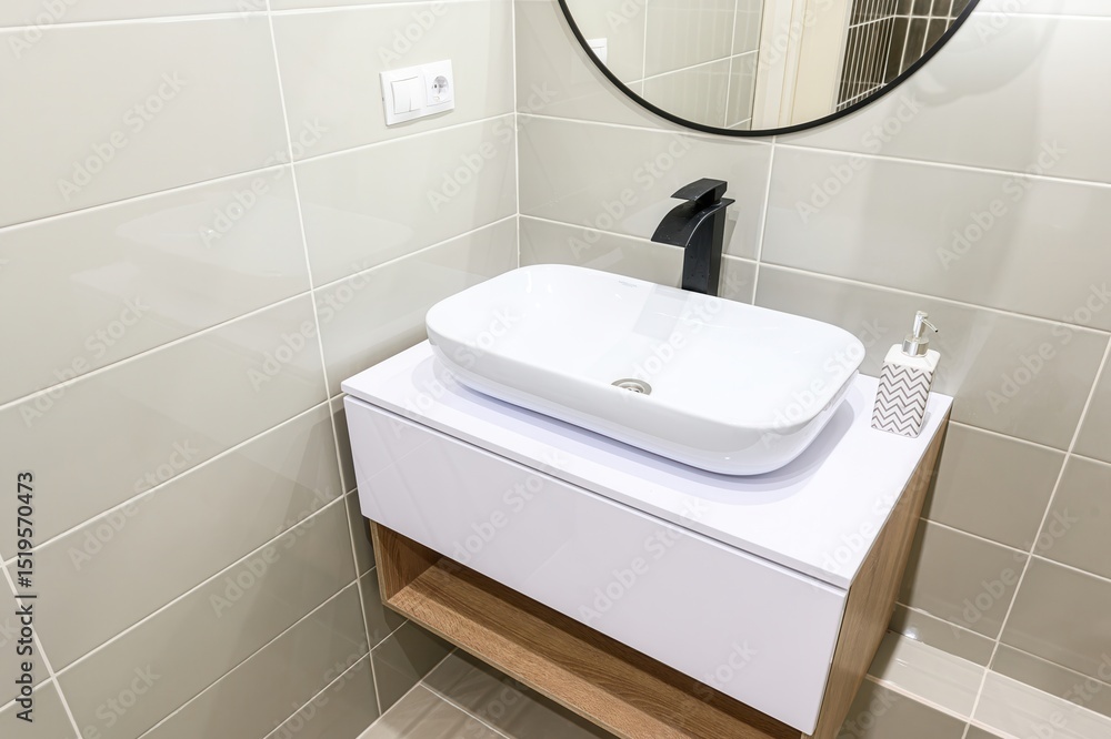 Fototapeta premium modern bathroom features a white rectangular sink, black faucet, and gray tiles. A round mirror hangs above