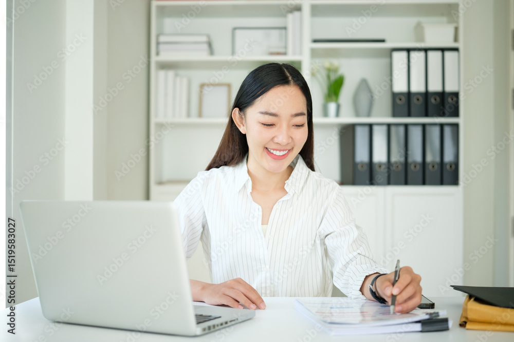 Young businesswoman smiling while working at a desk with documents and a laptop Young businesswoman smiling while working at a desk with documents and a laptop