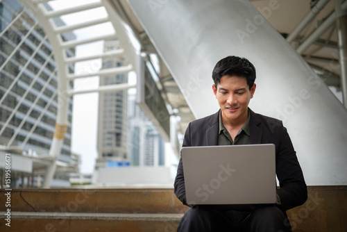 Wallpaper Mural Asian businessman in suit using a laptop while seated in a high rise business district. Torontodigital.ca