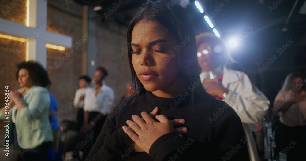 Fototapeta premium Women in prayer during church service, hands on chest in devotion, illuminated cross in the background, community gathering in spiritual reflection and worship