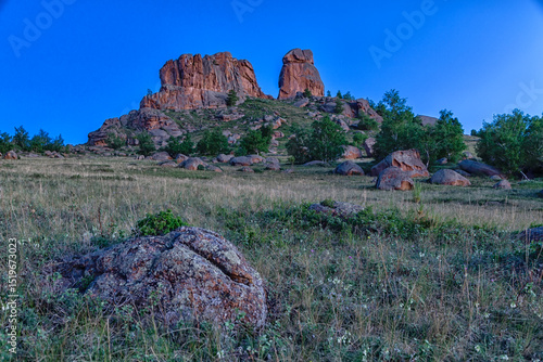 Two huge stone rocks in green jungle with lush vegetation at dawn in the blue hour without sharp shadows. Kazakh expanses, Mount Ku Egendybulak. Summer autumn landscape