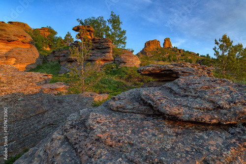 Huge stone standing rocks in green jungle with lush vegetation at dawn flooded with morning sun. Kazakh expanses, Mount Ku Egendybulak. Summer autumn landscape