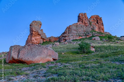 Early in the morning against the background of a blue clear sky without clouds a huge lonely rock with a large stone in the foreground. summer autumn landscape against the sun at sunset or sunrise