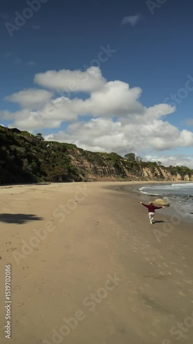 A very happy woman running along the beach near the stormy ocean, surrounded by mighty rocks, with a clear blue sky in the background.