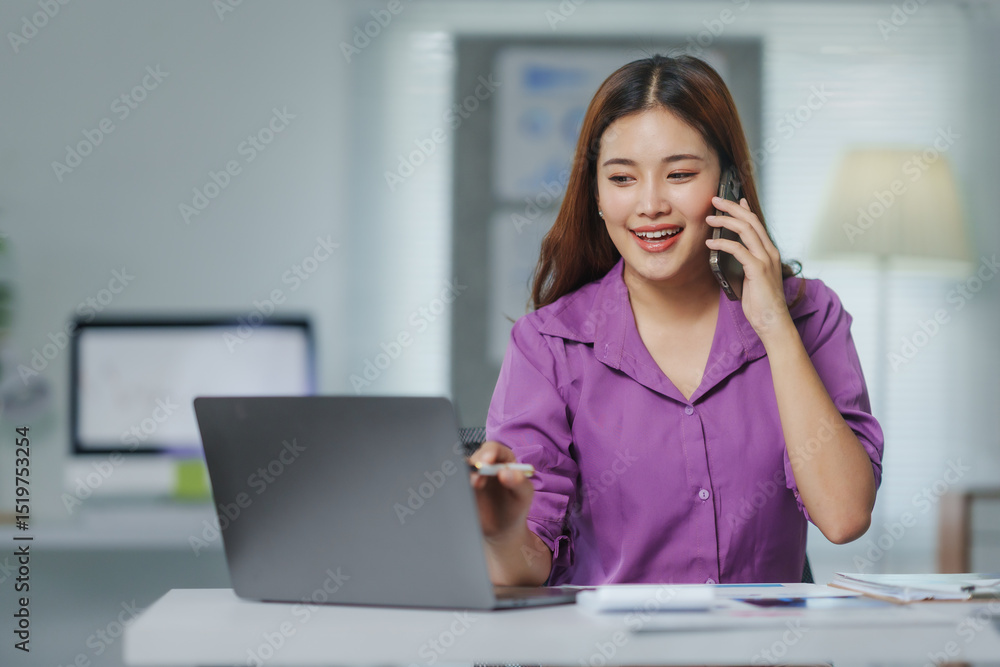 Young, happy Asian businesswoman talking on the phone while working on a laptop in a modern office, exuding professionalism and positivity Young, happy Asian businesswoman talking on the phone while working on a laptop in a modern office, exuding professionalism and positivity