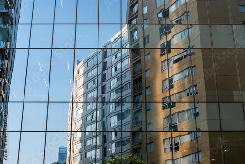 High-rise residential buildings mirrored on modern glass wall in Mexico City, captured from street level with urban density and light geometry for commercial design themes.