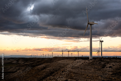 Sunset over wind farm in Zaragoza with clean ground line and atmospheric sky, excellent for sustainable themes and design applications with open space.