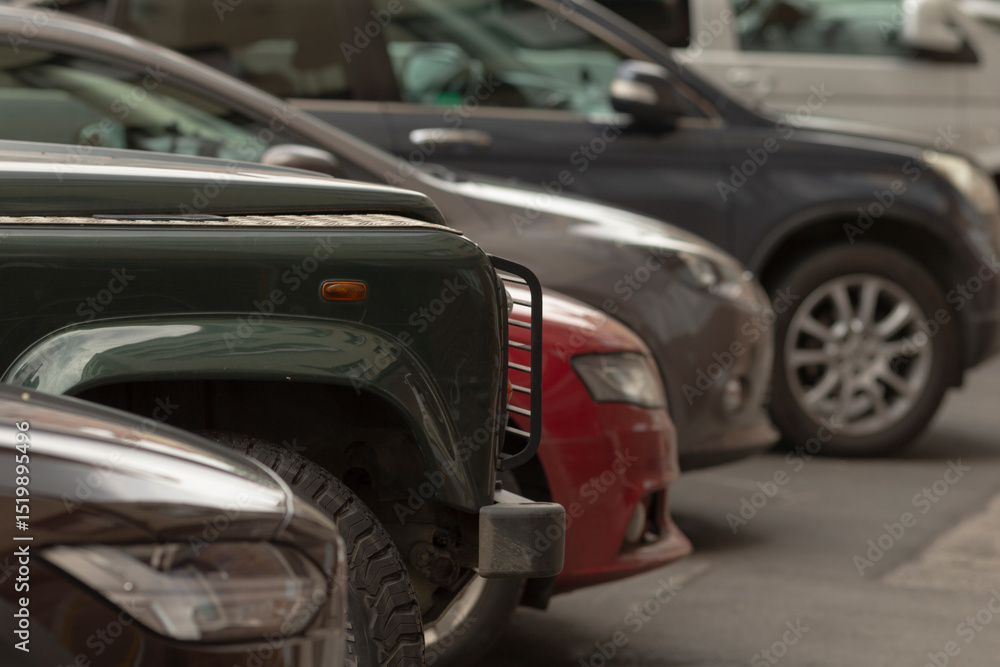 Fototapeta premium There is a long row of parked vehicles located within an urban area, showcasing a wide and diverse array of car models and colors, all positioned very closely to one another in proximity