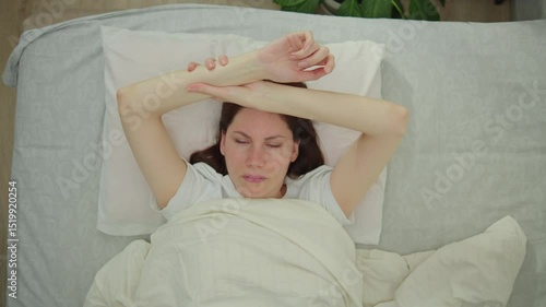 Young adult woman lies in bed in the morning and rubs her hand, who is numb after sleeping in an uncomfortable position