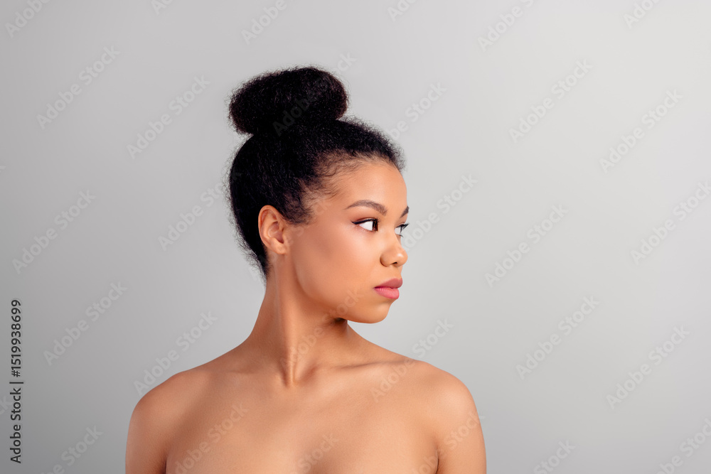 Obraz premium Elegant young woman with stylish bun hairstyle posing against a white background, showcasing natural beauty