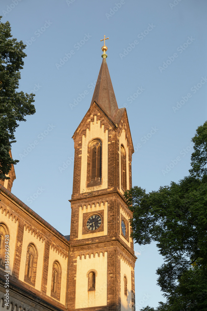 The tall church tower with a prominent clock stands elegantly among lush trees, beautifully illuminated by sunset, showcasing intricate details and its rich historical significance The tall church tower with a prominent clock stands elegantly among lush trees, beautifully illuminated by sunset, showcasing intricate details and its rich historical significance