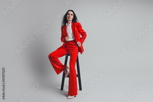 Konstfotografi Elegant young businesswoman in a stylish red suit seated against a neutral backg