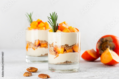 Trifle with persimmon, rosemary, pecan, whipped coconut cream and biscuit in a glasses. Healthy food, vegan, sugar, gluten and lactose free.