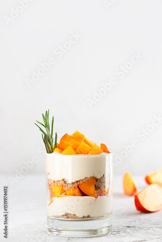 Dessert in a glass with persimmon, rosemary, pecan, whipped coconut cream. Healthy food, vegan, sugar, gluten and lactose free. Vertical orientation.