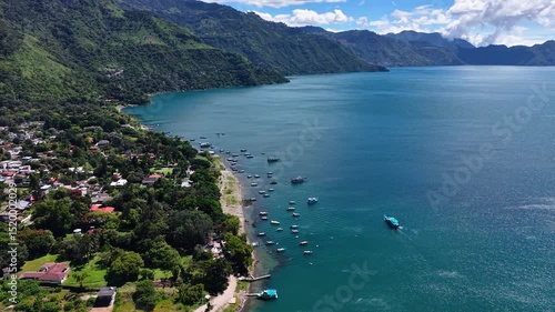 Cinematic aerial view over Lake Atitlán revealing San Juan La Laguna's iconic piers, colorful boats, and the towering volcanoes that dominate the Guatemalan highlands