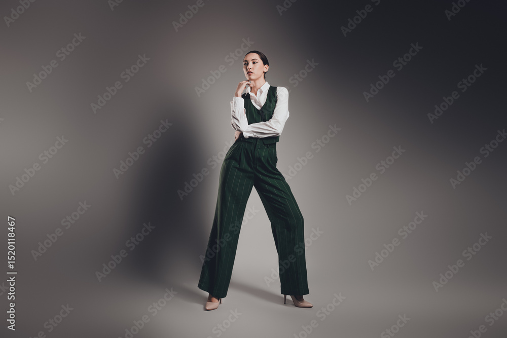 Confident Businesswoman in Elegant Green Suit Posing Against Grey Background in Studio Setting Confident Businesswoman in Elegant Green Suit Posing Against Grey Background in Studio Setting