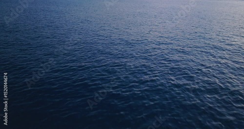 Aerial shot over a magical ocean surface during sunset. Calm, deep blue sea at dusk.