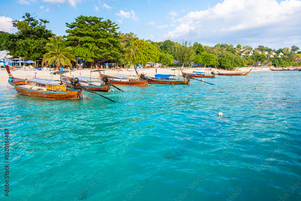 Obraz premium Crystal clear turquoise water gently laps the shore of Long Beach in Phi Phi Don, Thailand, where traditional longtail boats are moored, creating a serene and picturesque scene