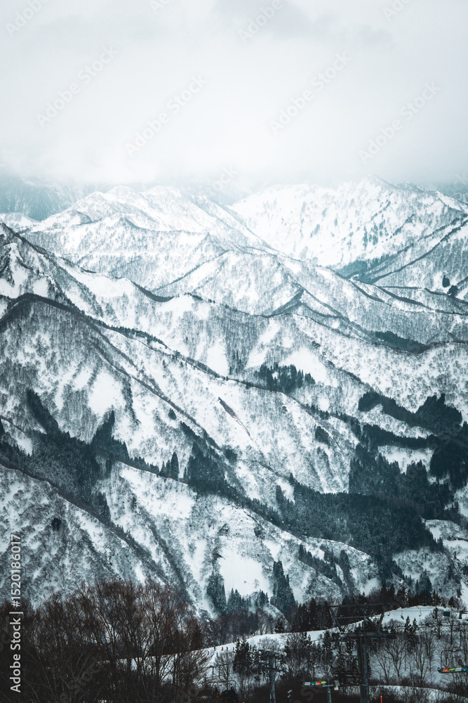Obraz premium A breathtaking panoramic view of snow-covered mountain ranges including Ishiuchi Maruyama, Yuzawa Kogen, and distant peaks near Echigo-Yuzawa in Niigata, Japan, captured from Gala Yuzawa station.