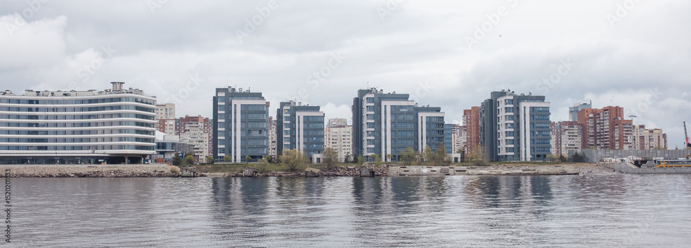 Fototapeta premium Modern Waterfront Buildings Line the Neva River in St. Petersburg During a Cloudy Day in the Spring