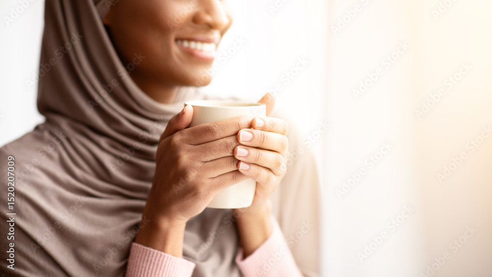 Cropped view of happy black woman in hijab warming her hands on cup of hot coffee near window at home. Lovely young Muslim lady having relaxing morning with aromatic drink, enjoying her break Cropped view of happy black woman in hijab warming her hands on cup of hot coffee near window at home. Lovely young Muslim lady having relaxing morning with aromatic drink, enjoying her break