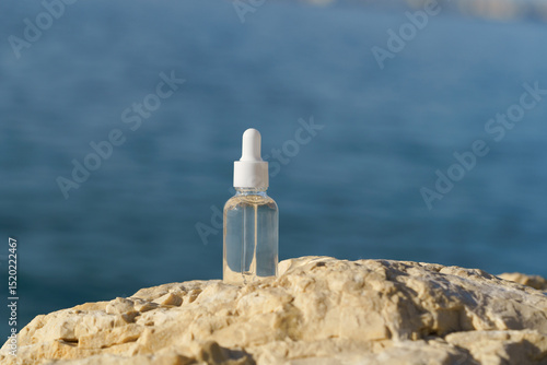 Transparent glass jar of serum with pipette dispenser for facial skin on stone on sea background. Concept of natural cosmetics beauty, facial skin care, moisturizing and revitalization