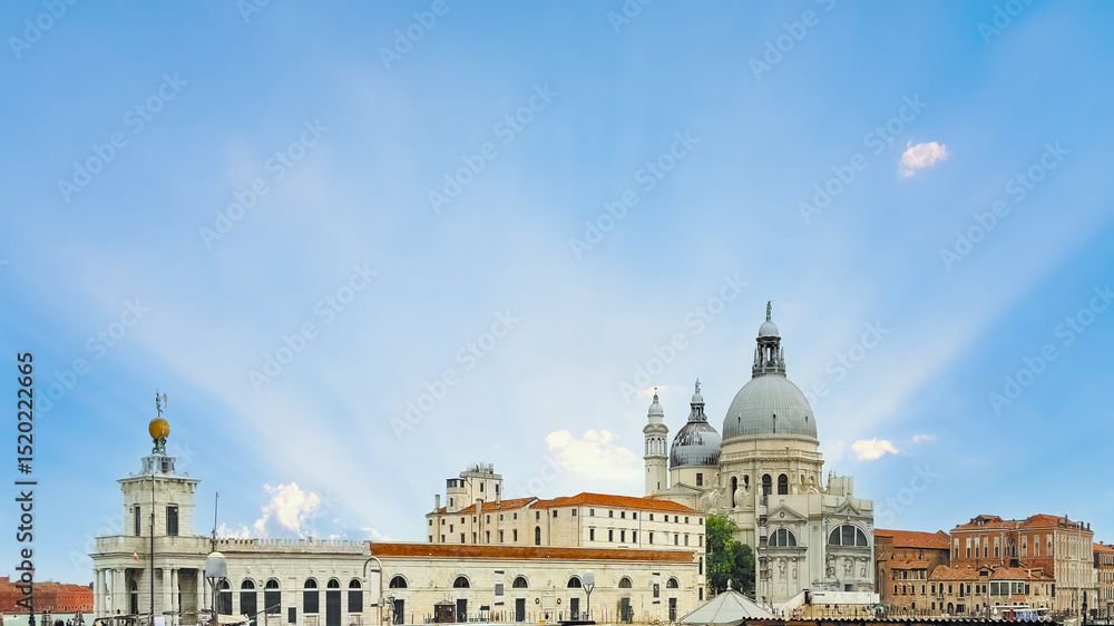 Obraz premium Sun rays illuminate the iconic Santa Maria della Salute basilica and historic Venetian architecture under a beautiful blue sky, a famous travel destination and landmark in Venice, Italy