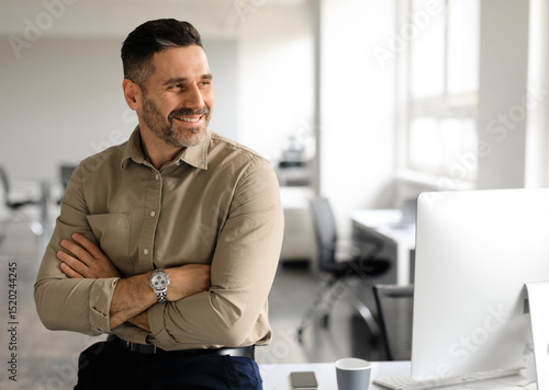 Happy middle aged businessman standing by his workplace, looking aside at copy space, thinking of new startup or project, smiling at good thoughts, planning investment, enjoying success