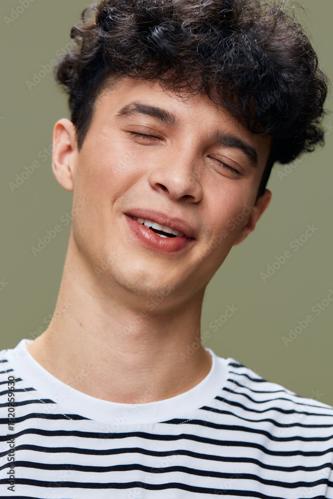 Fototapeta premium smiling man with curly hair wearing striped shirt, eyes closed, joyful expression, casual style, simple green background, natural light portrait